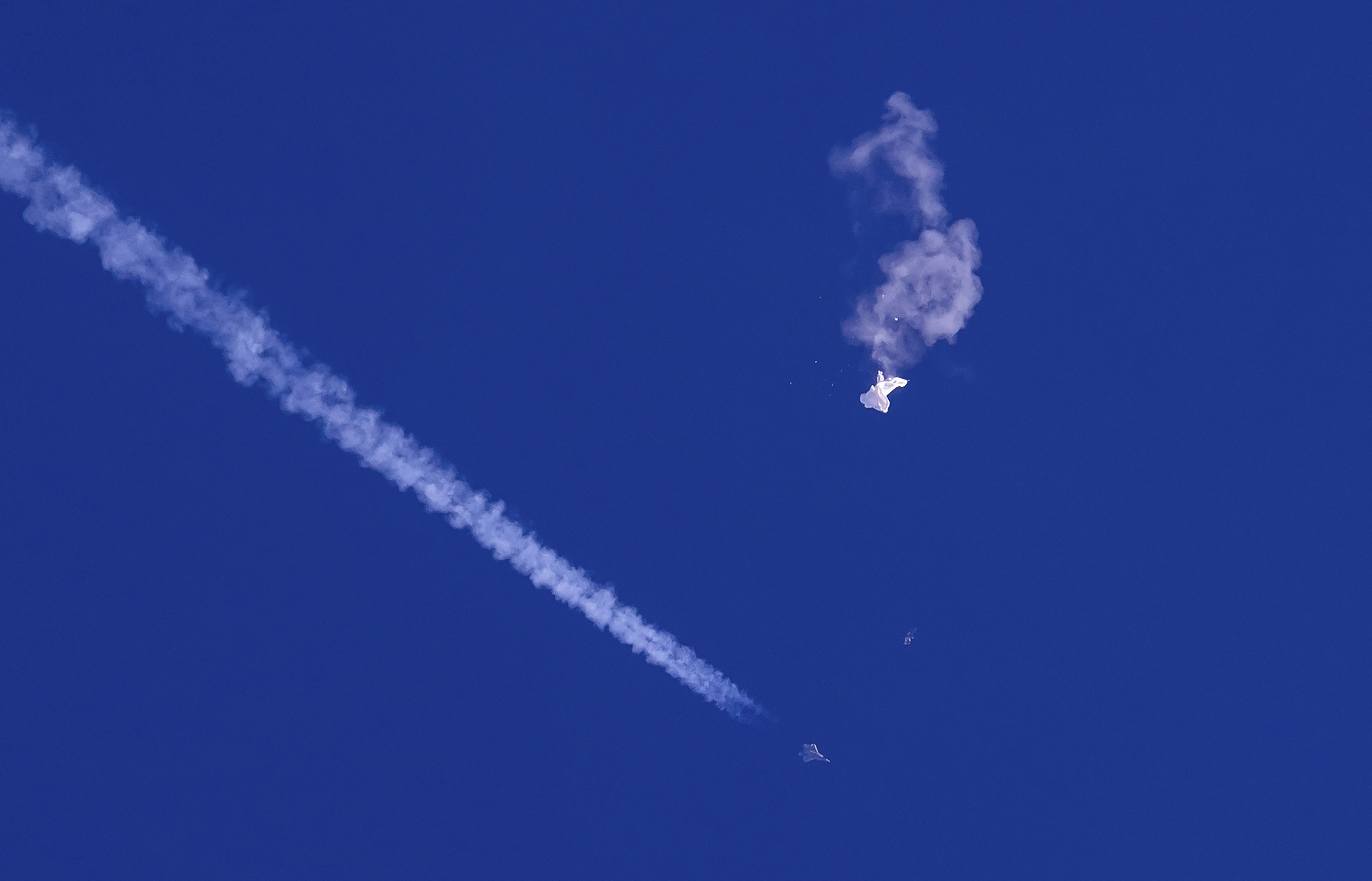 In this photo provided by Chad Fish, the remnants of a large balloon drift above the Atlantic Ocean, just off the coast of South Carolina, with a fighter jet and its contrail seen below it, Feb. 4, 2023.